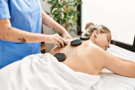 Photo for Woman couple having back treatment using hot black stones at beauty center - Royalty Free Image