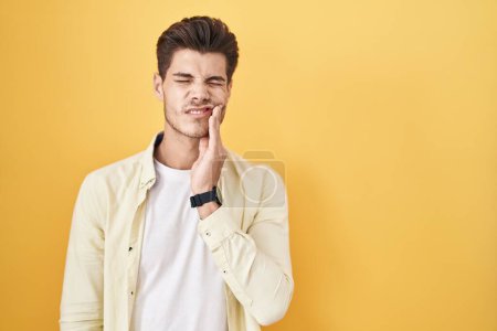 Photo for Young hispanic man standing over yellow background touching mouth with hand with painful expression because of toothache or dental illness on teeth. dentist - Royalty Free Image