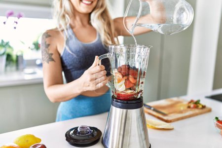 Photo for Young woman smiling confident pouring water on blender at kitchen - Royalty Free Image
