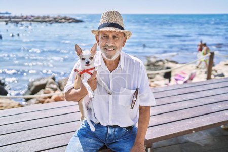 Photo for Senior man wearing summer hat hugging chihuahua at seaside - Royalty Free Image