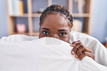 Foto de Mujer afroamericana cubriendo la boca acostada en la cama en el dormitorio - Imagen libre de derechos