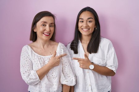 Photo for Hispanic mother and daughter together cheerful with a smile on face pointing with hand and finger up to the side with happy and natural expression - Royalty Free Image
