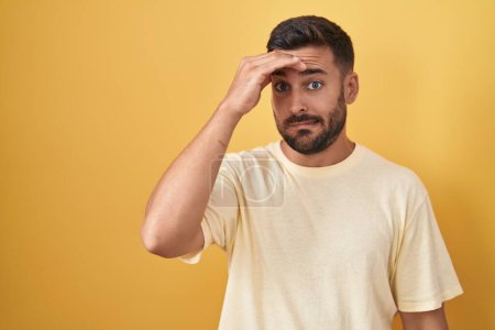 Photo for Handsome hispanic man standing over yellow background worried and stressed about a problem with hand on forehead, nervous and anxious for crisis - Royalty Free Image