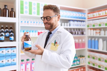 Photo for Middle age man pharmacist smiling confident holding medication bottle at pharmacy - Royalty Free Image