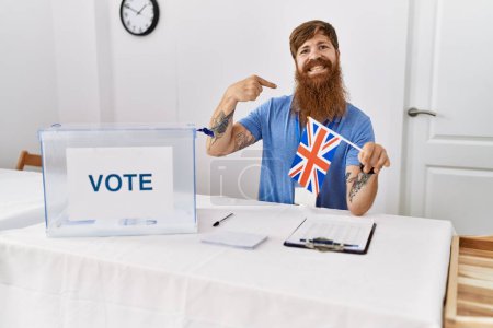 Téléchargez les photos : Homme caucasien avec une longue barbe à l'élection de la campagne politique tenant drapeau britannique pointant du doigt un sourire heureux et fier - en image libre de droit