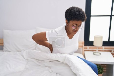 Foto de Mujer afroamericana sufriendo por lesión de rodilla sentada en la cama en el dormitorio - Imagen libre de derechos