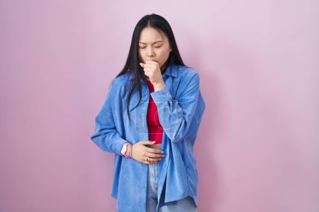 Foto de Mujer asiática joven de pie sobre fondo rosado sintiéndose mal y tosiendo como síntoma de resfriado o bronquitis. concepto de atención sanitaria. - Imagen libre de derechos
