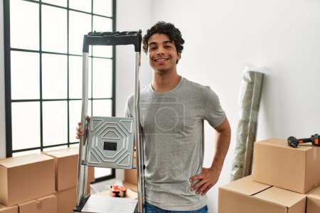 Photo for Young hispanic man smiling happy holding ladder at new home. - Royalty Free Image