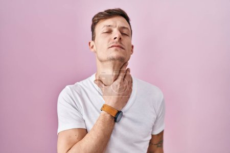 Foto de Hombre caucásico de pie sobre fondo rosa tocando el cuello doloroso, dolor de garganta para la gripe, la clod y la infección - Imagen libre de derechos