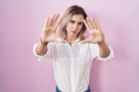 Photo for Young beautiful woman standing over pink background doing frame using hands palms and fingers, camera perspective - Royalty Free Image