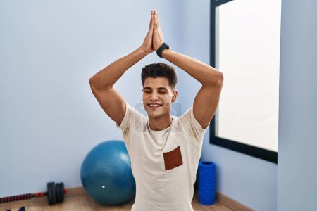 Téléchargez les photos : Jeune homme hispanique souriant entraînement confiant yoga au centre sportif - en image libre de droit