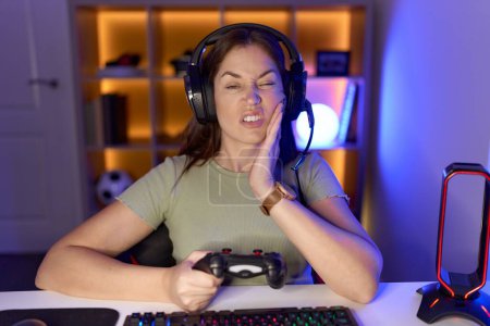 Photo for Beautiful brunette woman playing video games wearing headphones touching mouth with hand with painful expression because of toothache or dental illness on teeth. dentist concept. - Royalty Free Image