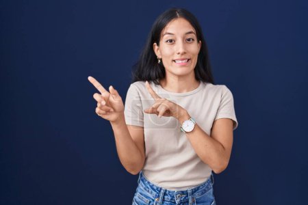 Téléchargez les photos : Jeune femme hispanique debout sur fond bleu pointant de côté inquiet et nerveux avec les deux mains, préoccupé et expression surprise - en image libre de droit