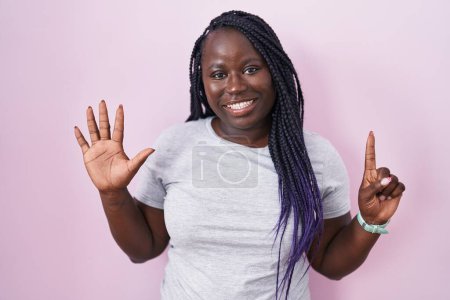 Foto de Joven mujer africana de pie sobre fondo rosa mostrando y señalando hacia arriba con los dedos número seis mientras sonríe confiado y feliz. - Imagen libre de derechos