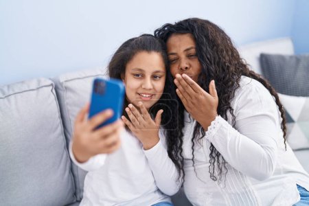 Téléchargez les photos : Mère et fille ayant un appel vidéo assis sur le canapé à la maison - en image libre de droit