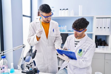 Foto de Dos hombres científicos sosteniendo tubos de ensayo escriben en portapapeles trabajando en laboratorio - Imagen libre de derechos
