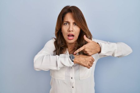 Photo for Hispanic woman standing over isolated background in hurry pointing to watch time, impatience, upset and angry for deadline delay - Royalty Free Image