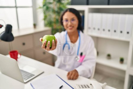 Photo for Young latin woman wearing doctor uniform holding apple at clinic - Royalty Free Image