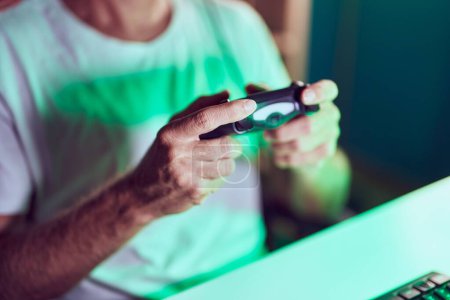 Téléchargez les photos : Jeune homme blond streamer jouer à un jeu vidéo en utilisant joystick à la salle de jeu - en image libre de droit