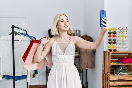 Téléchargez les photos : Young caucasian woman holding shopping bags make selfie by the smartphone at clothing store - en image libre de droit