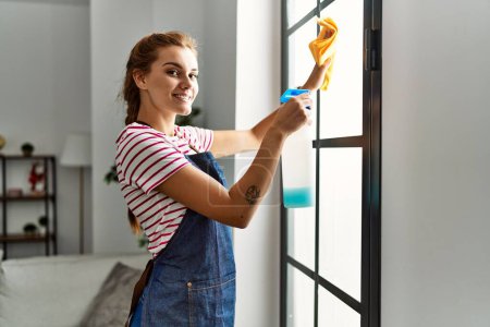 Foto de Mujer joven sonriendo confiada ventana de limpieza en casa - Imagen libre de derechos