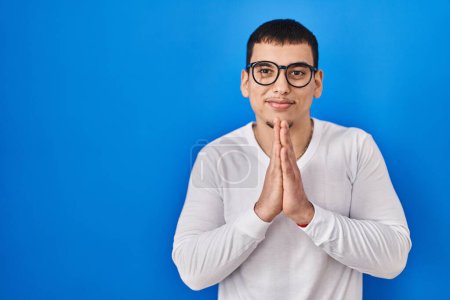 Photo for Young arab man wearing casual white shirt and glasses praying with hands together asking for forgiveness smiling confident. - Royalty Free Image
