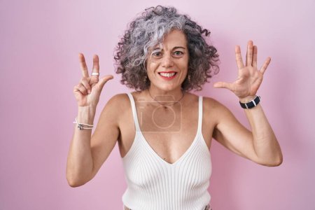 Foto de Mujer de mediana edad con el pelo gris de pie sobre el fondo rosa que muestra y señala hacia arriba con los dedos número ocho mientras sonríe confiado y feliz. - Imagen libre de derechos