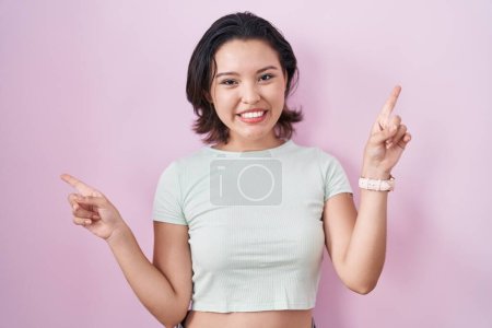 Foto de Mujer joven hispana de pie sobre fondo rosa sonriendo confiada señalando con los dedos a diferentes direcciones. espacio de copia para publicidad - Imagen libre de derechos