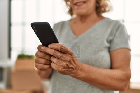 Photo for Middle age caucasian woman smiling happy using smartphone at new home. - Royalty Free Image