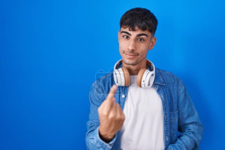 Téléchargez les photos : Young hispanic man standing over blue background beckoning come here gesture with hand inviting welcoming happy and smiling - en image libre de droit