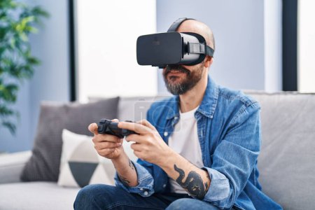 Foto de Joven calvo jugando videojuego usando gafas de realidad virtual en casa - Imagen libre de derechos