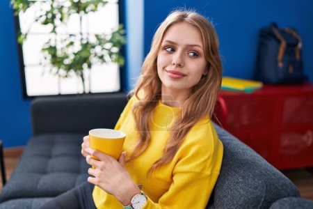 Téléchargez les photos : Young blonde woman drinking coffee sitting on sofa at street - en image libre de droit