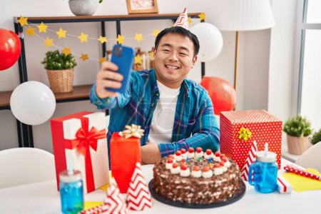 Foto de Young chinese man celebrating birthday make selfie by smartphone at home - Imagen libre de derechos