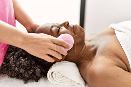 Photo for African american woman lying on massage table having facial treatment at beauty salon - Royalty Free Image