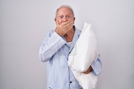 Photo for Senior man with grey hair wearing pijama hugging pillow laughing and embarrassed giggle covering mouth with hands, gossip and scandal concept - Royalty Free Image