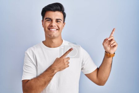 Photo for Hispanic man standing over blue background smiling and looking at the camera pointing with two hands and fingers to the side. - Royalty Free Image