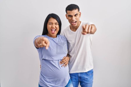 Photo for Young hispanic couple expecting a baby standing over background pointing displeased and frustrated to the camera, angry and furious with you - Royalty Free Image