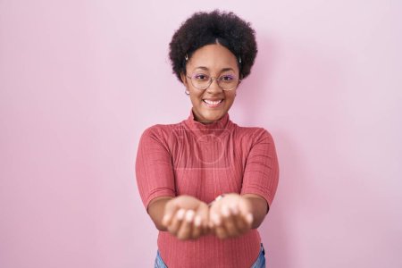 Photo for Beautiful african woman with curly hair standing over pink background smiling with hands palms together receiving or giving gesture. hold and protection - Royalty Free Image