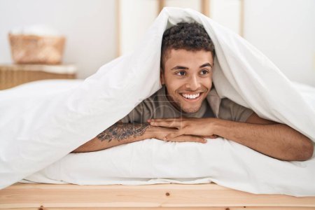 Téléchargez les photos : Afro-Américain couché sur le lit couvrant avec drap de lit dans la chambre - en image libre de droit
