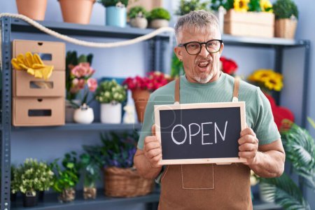 Photo for Hispanic man with grey hair working at florist holding open sign clueless and confused expression. doubt concept. - Royalty Free Image