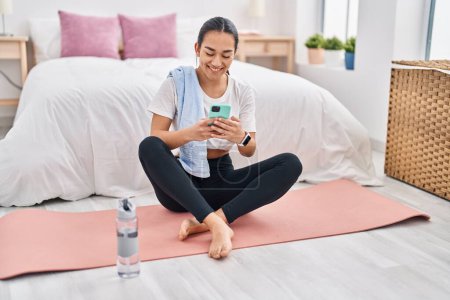 Photo for Young hispanic woman using smartphone sitting on floor at bedroom - Royalty Free Image