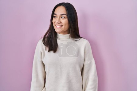 Photo for Young south asian woman standing over pink background looking away to side with smile on face, natural expression. laughing confident. - Royalty Free Image