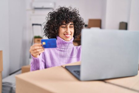 Foto de Joven mujer de Oriente Medio utilizando el ordenador portátil y tarjeta de crédito en el nuevo hogar - Imagen libre de derechos