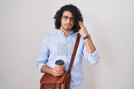 Foto de Hombre hispano con el pelo rizado bebiendo una taza de café para llevar disparando y matándose apuntando con la mano y los dedos a la cabeza como arma, gesto suicida. - Imagen libre de derechos