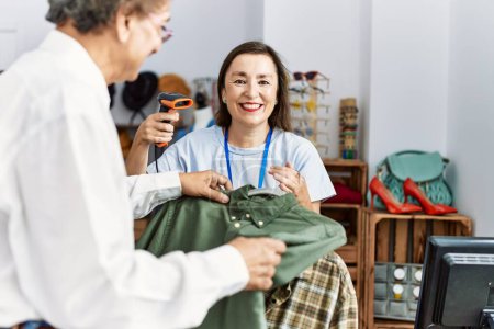 Foto de Hombre y mujer de mediana edad sonriendo confiados escaneando ropa usando lector de código de barras en la tienda de ropa - Imagen libre de derechos