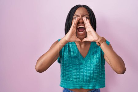 Photo for Young african american with braids standing over pink background shouting angry out loud with hands over mouth - Royalty Free Image