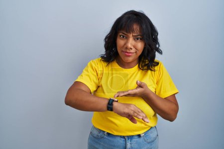 Photo for Hispanic woman standing over blue background in hurry pointing to watch time, impatience, upset and angry for deadline delay - Royalty Free Image
