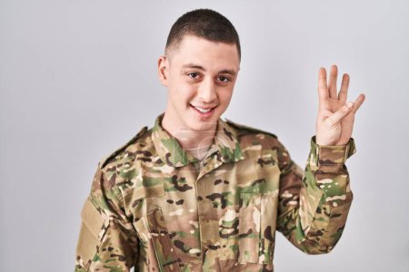 Photo for Young man wearing camouflage army uniform showing and pointing up with fingers number four while smiling confident and happy. - Royalty Free Image
