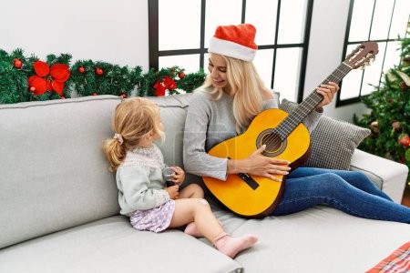Téléchargez les photos : Mother and daughter playing guitar and singing sitting by christmas tree at home - en image libre de droit