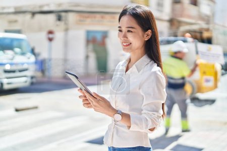 Téléchargez les photos : Jeune femme chinoise souriant confiant en utilisant touchpad à la rue - en image libre de droit